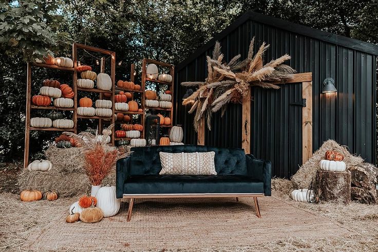 a couch sitting in front of a black shed with pumpkins on the ground and hay bales behind it