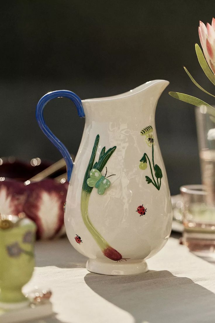 a white vase with flowers painted on it sitting on a table next to other glassware