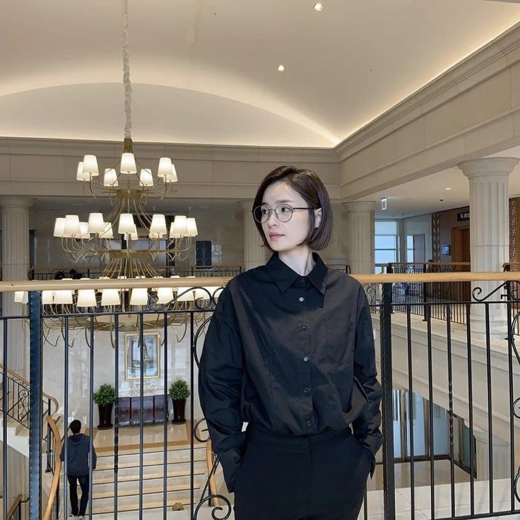 a woman standing in front of a chandelier and railing with her hands on her hips