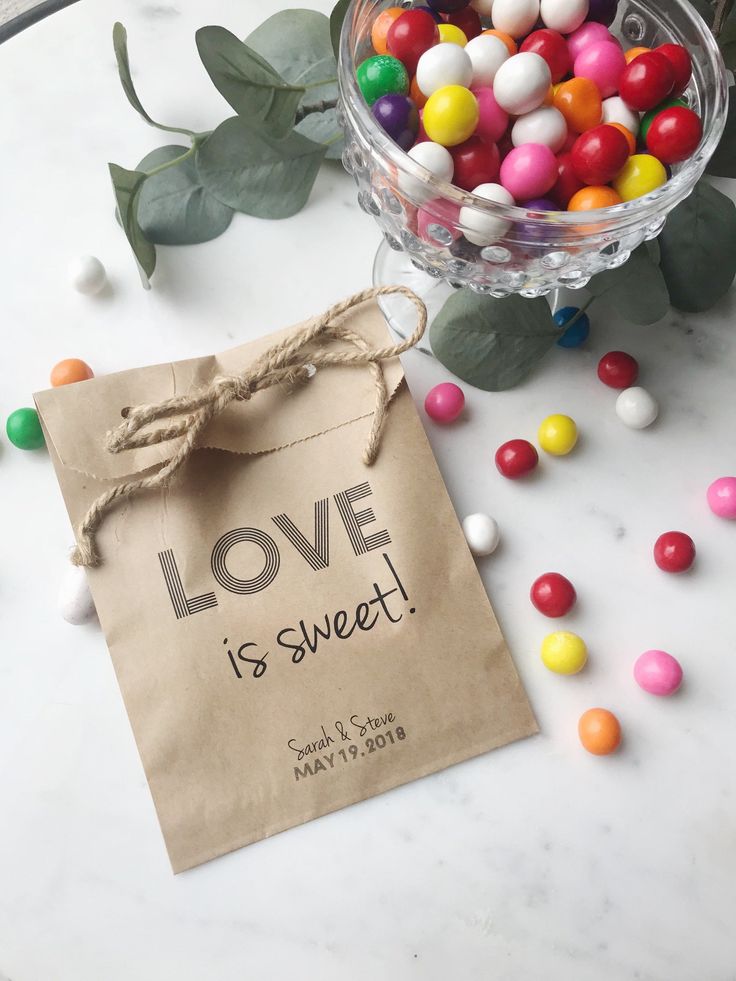 a bag with love is sweet written on it next to some candies and greenery