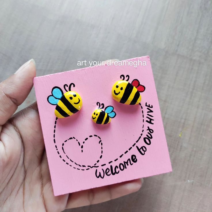 a hand holding a pink card with two yellow and black bee studs on it