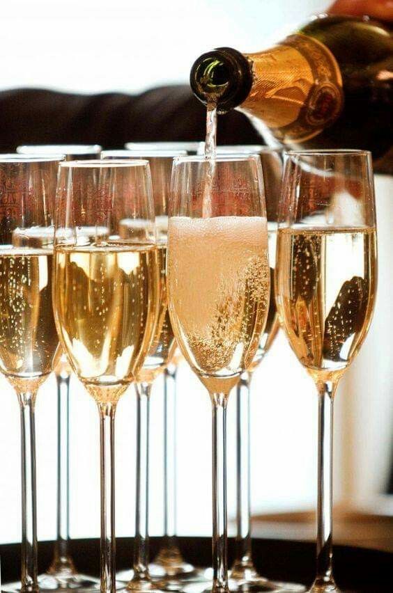 champagne being poured into wine glasses in front of another glass filled with white and gold liquid