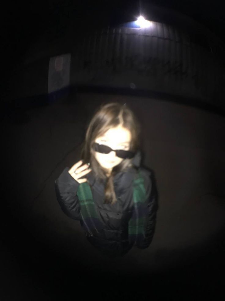 a woman wearing sunglasses is seen through the lens of her cell phone camera at night