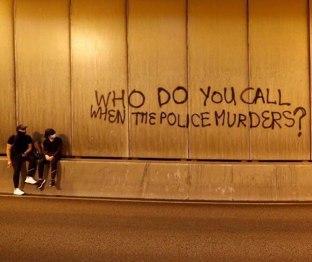 two people sitting against a wall with graffiti written on it that says who do you call when the police murders?