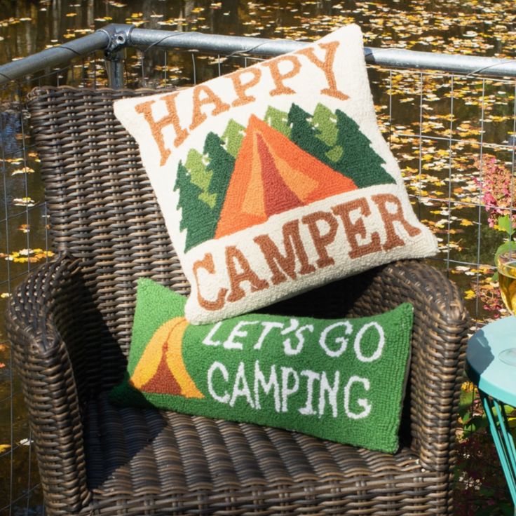 a happy camper pillow sitting on top of a wicker chair next to a table