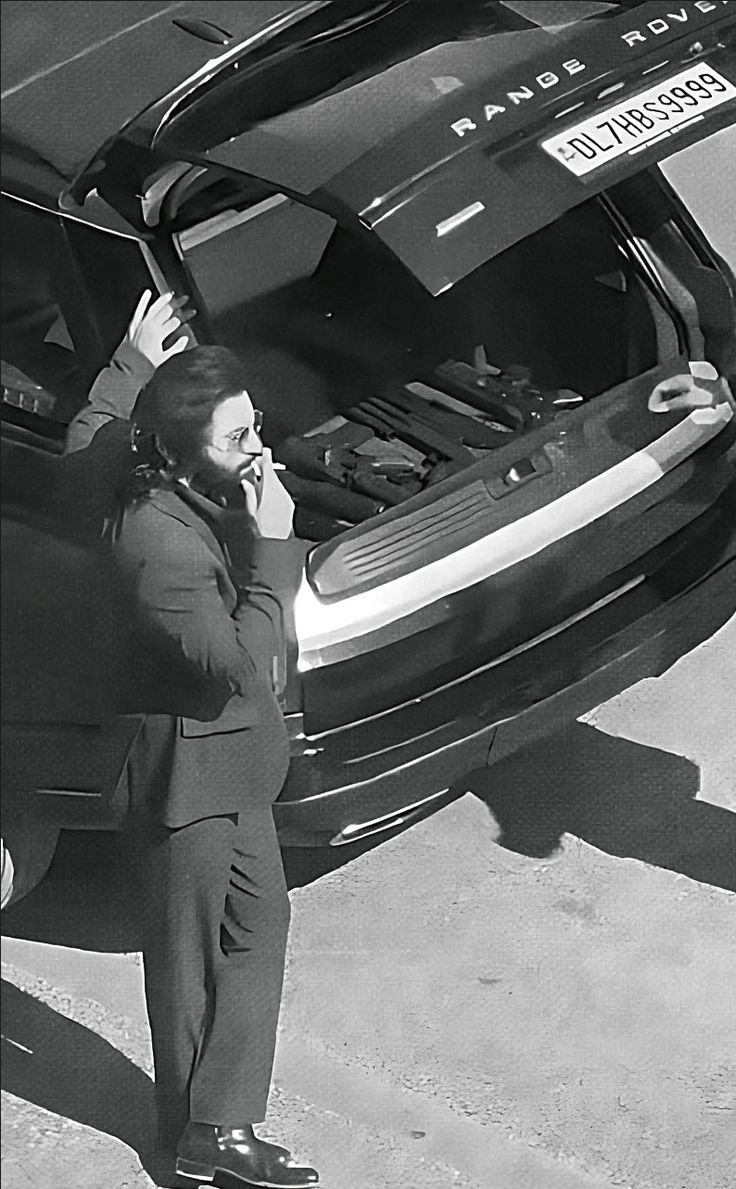 a woman standing next to a car talking on a cell phone while holding her trunk open