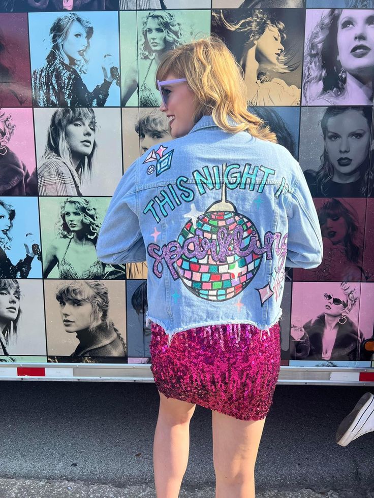 a woman standing in front of a wall with pictures on it and wearing a jean jacket