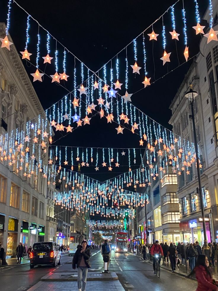 people are walking down the street with christmas lights