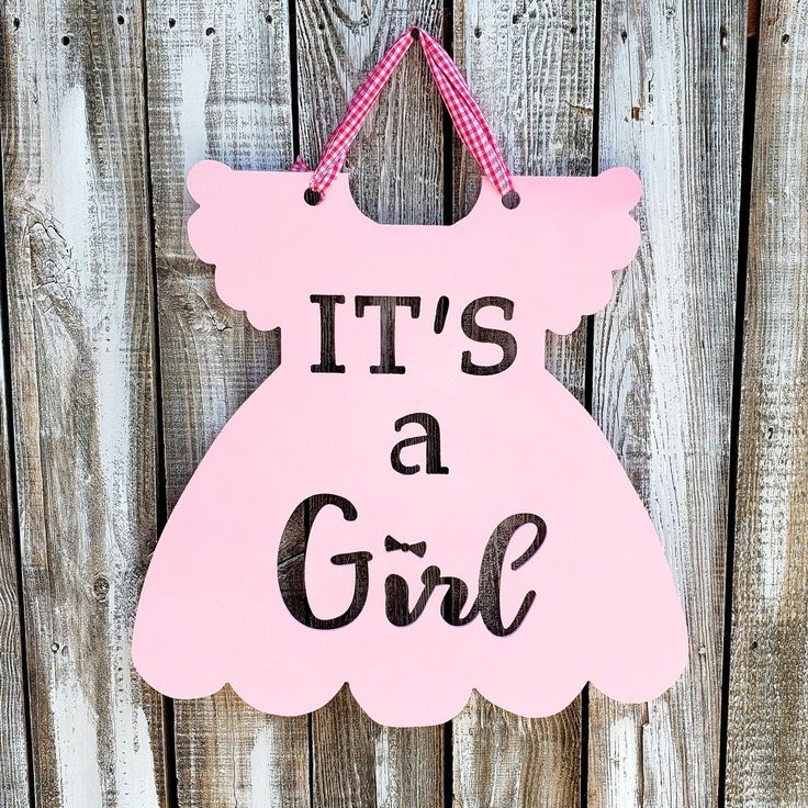 it's a girl door hanger with pink dress hanging from the side on a wooden fence