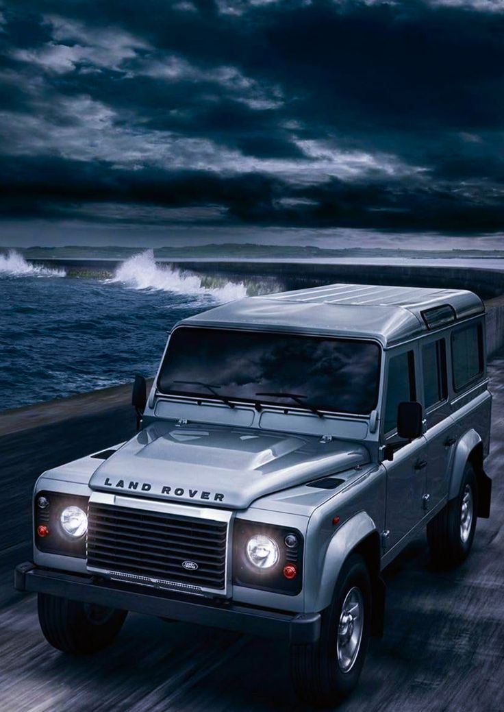 the land rover is driving down the road by the ocean at night with dark clouds