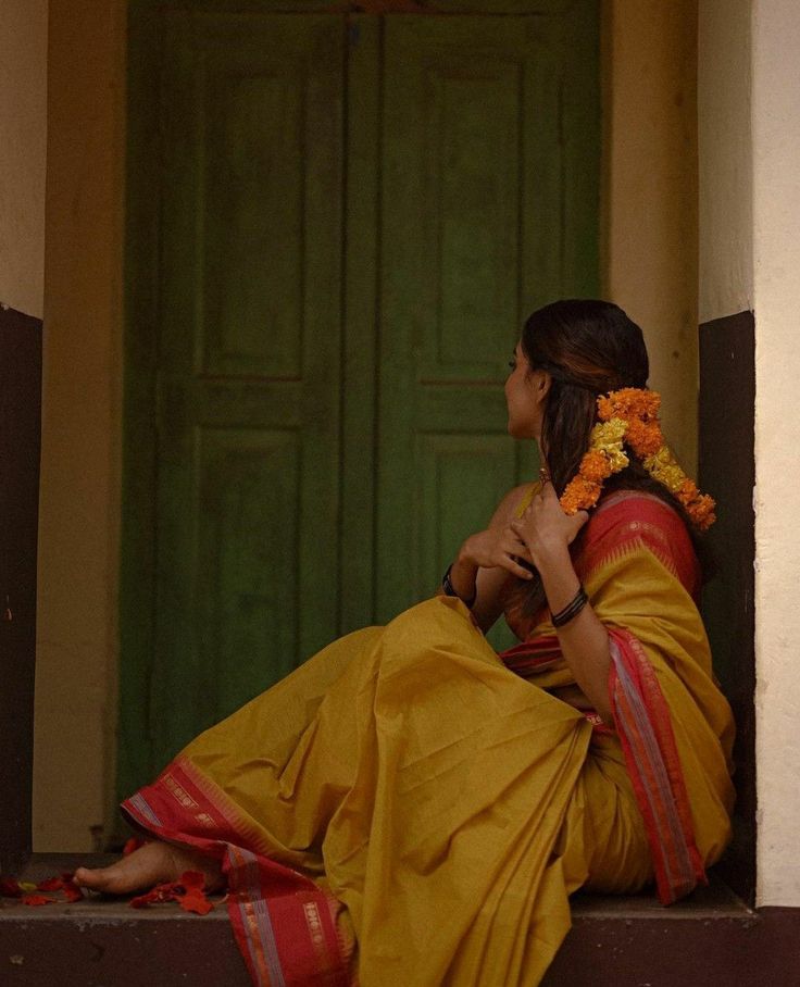 a woman sitting on the steps in front of a green door wearing a yellow sari