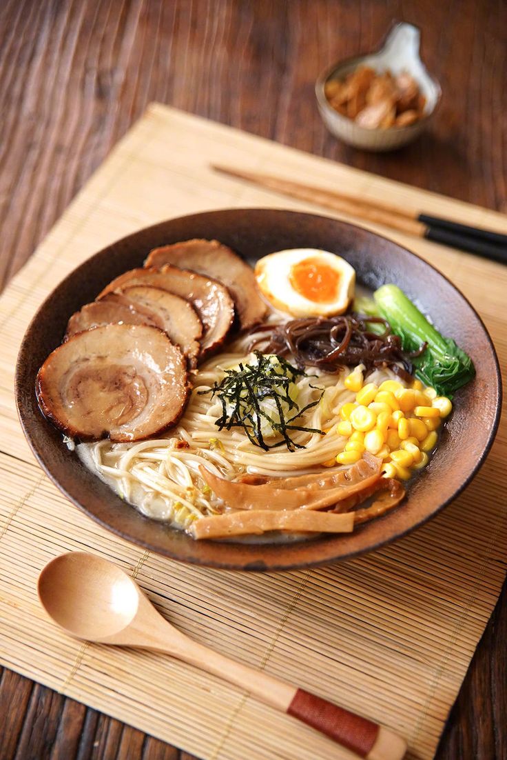 a bowl of ramen with meat, vegetables and an egg on the side next to chopsticks