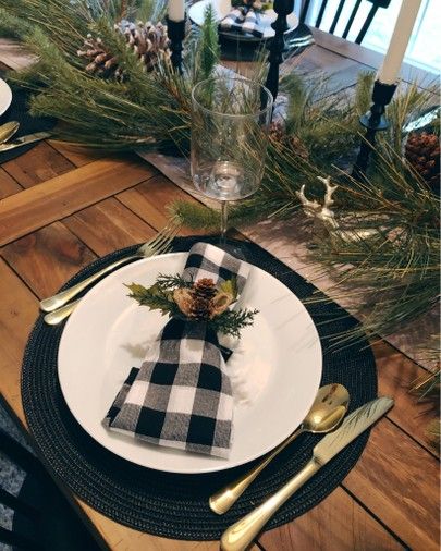 a black and white place setting with pine cones, greenery and plaid napkins