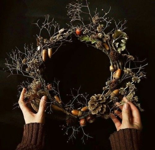 two hands holding up a wreath made out of branches and acorns