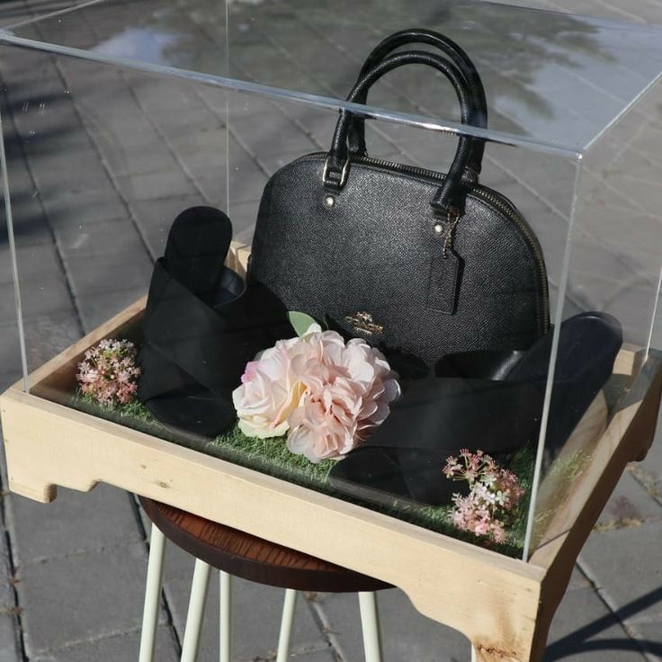 a handbag and hat sitting in a display case on a wooden table next to a black purse