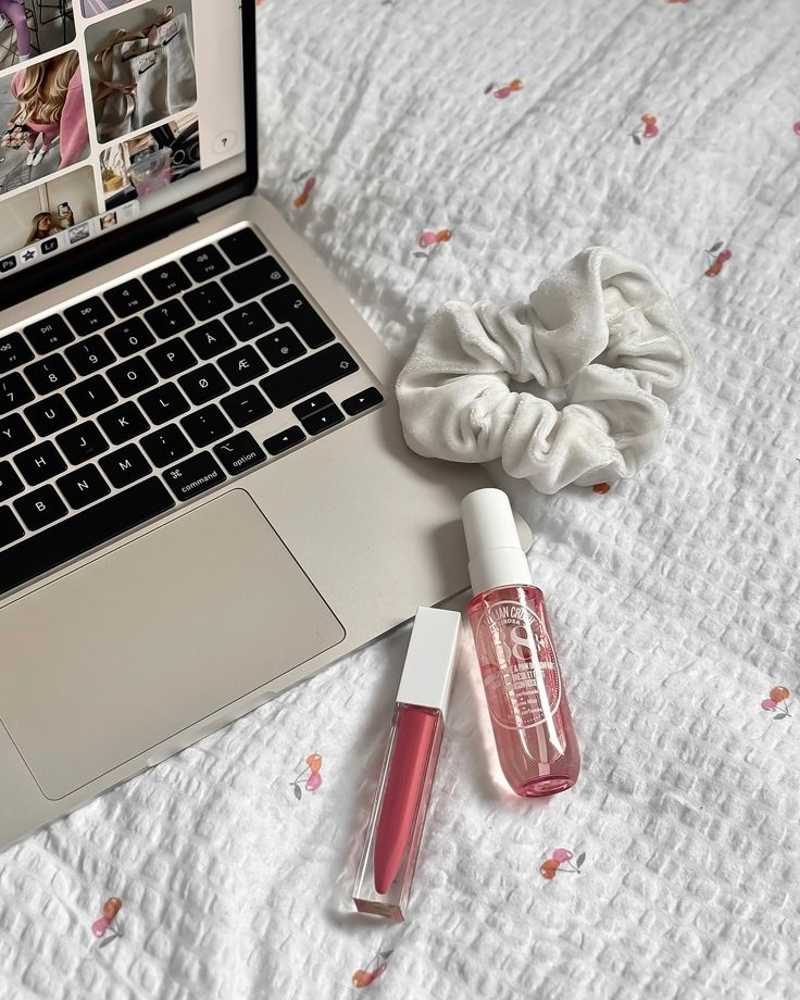 an open laptop computer sitting on top of a bed next to a bottle of lipstick