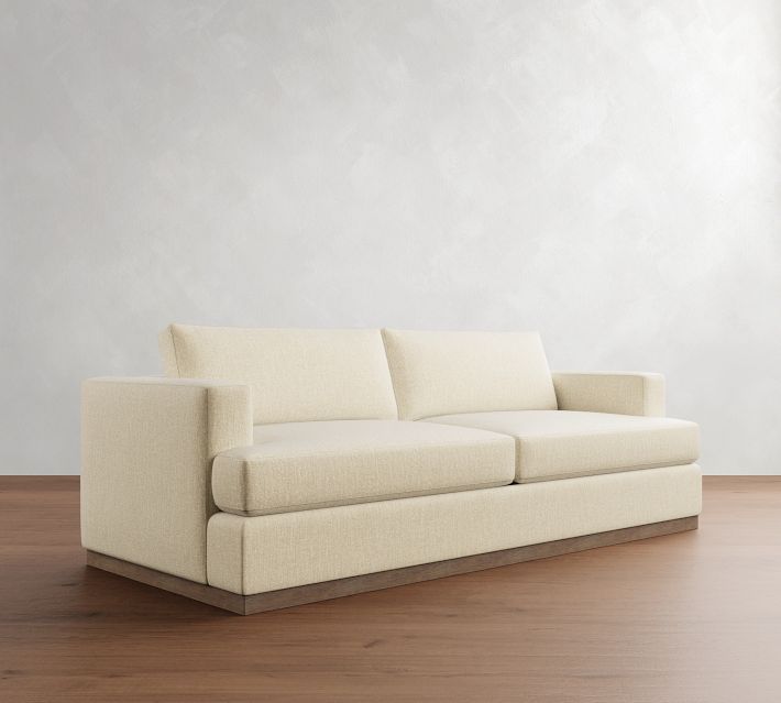 a white couch sitting on top of a wooden floor next to a wall and window