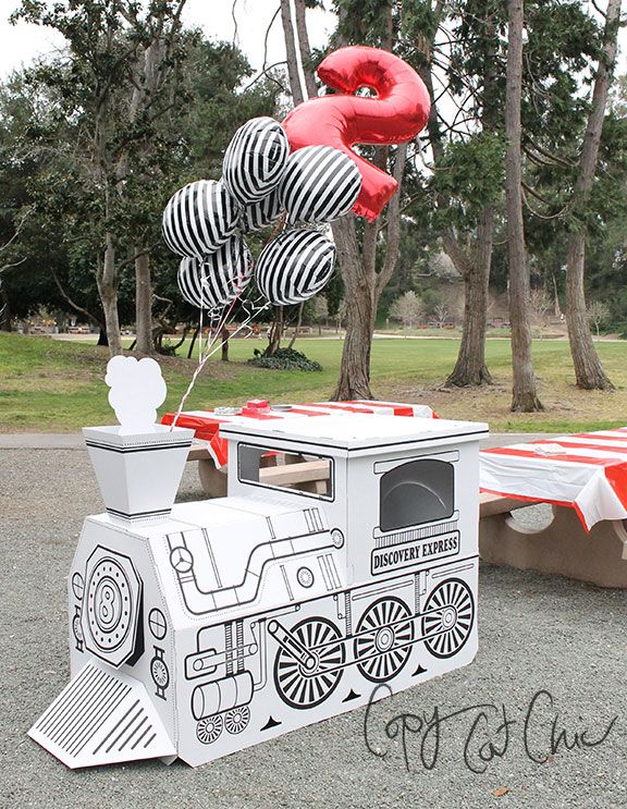 an ice cream cart with balloons in the shape of train cars is parked next to a picnic table