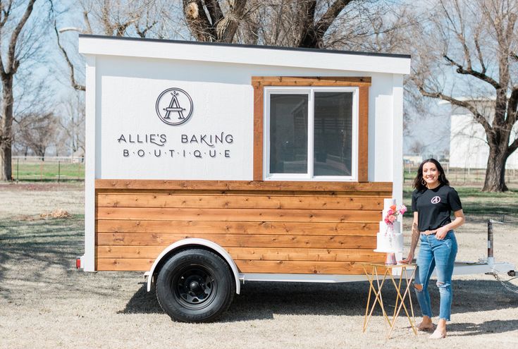 a woman standing in front of a small white and wood truck with the name allies'baking boutique on it