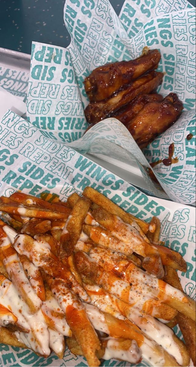 french fries with sauce and chicken wings in paper wrappers