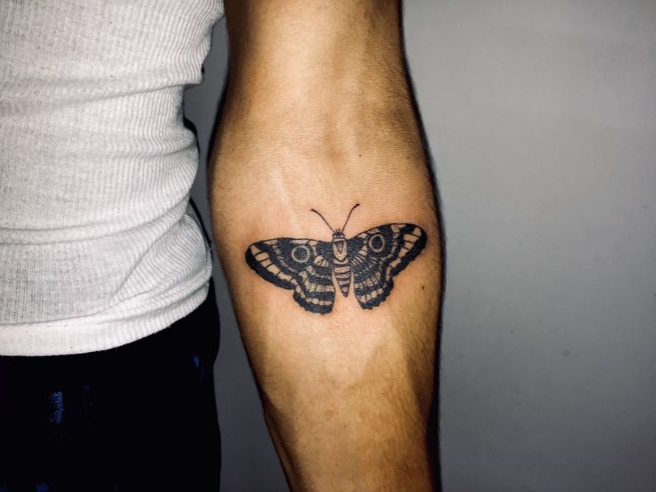 a small moth tattoo on the left arm and lower leg, next to a man's legs