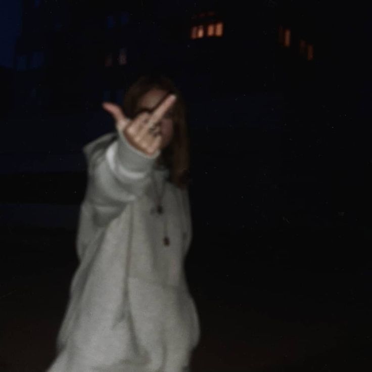 a woman is standing in the dark with her hand up and she is wearing a white coat