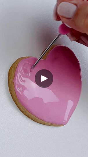 a heart shaped cookie being decorated with pink icing