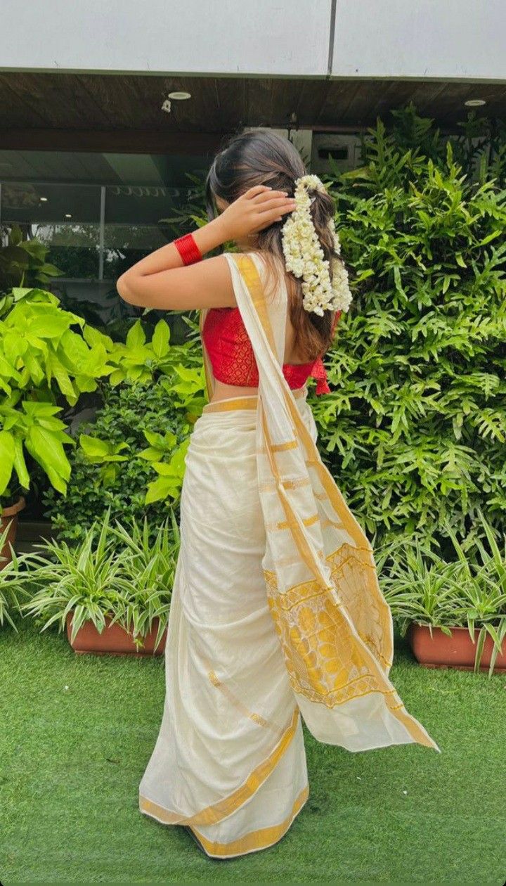 a woman wearing a white and yellow sari with flowers in her hair standing on grass