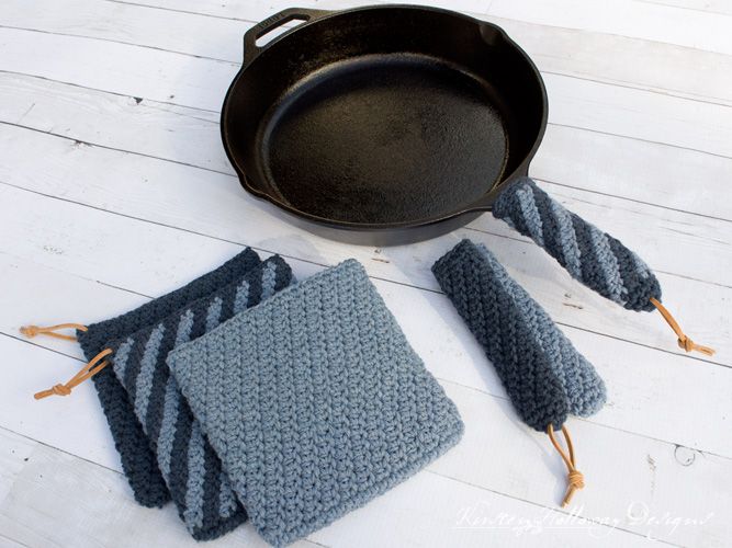 a cast iron skillet sitting on top of a wooden floor next to two knitted dishcloths