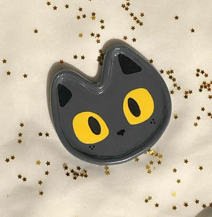 a black and yellow cat brooch sitting on top of a white sheet with gold stars