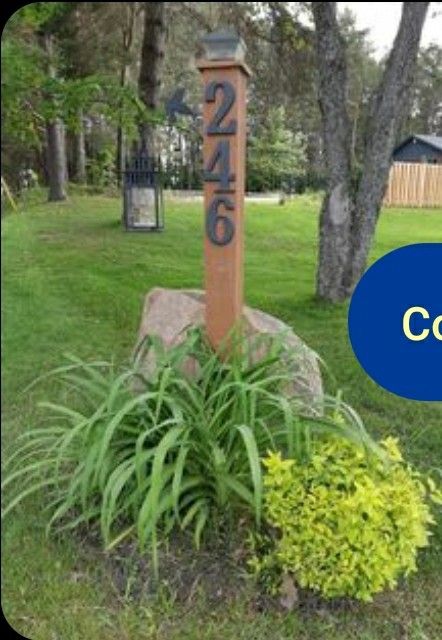 a wooden sign sitting in the middle of a lush green field next to a tree