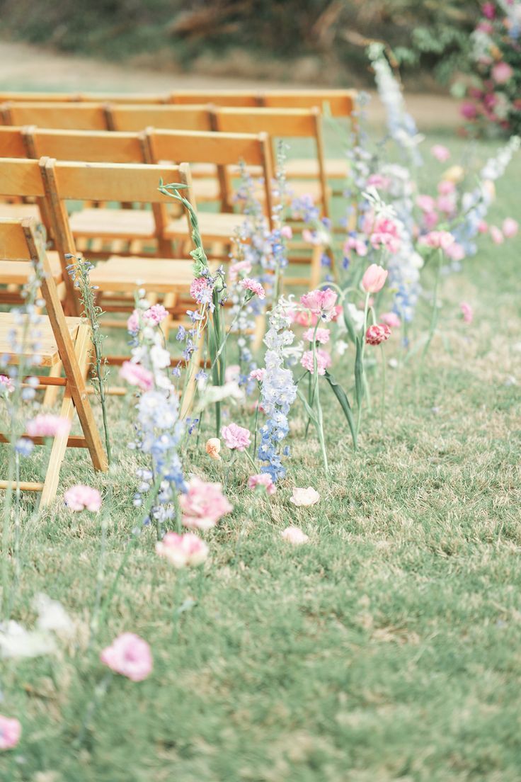 rows of wooden chairs sitting on top of a grass covered field next to pink and blue flowers