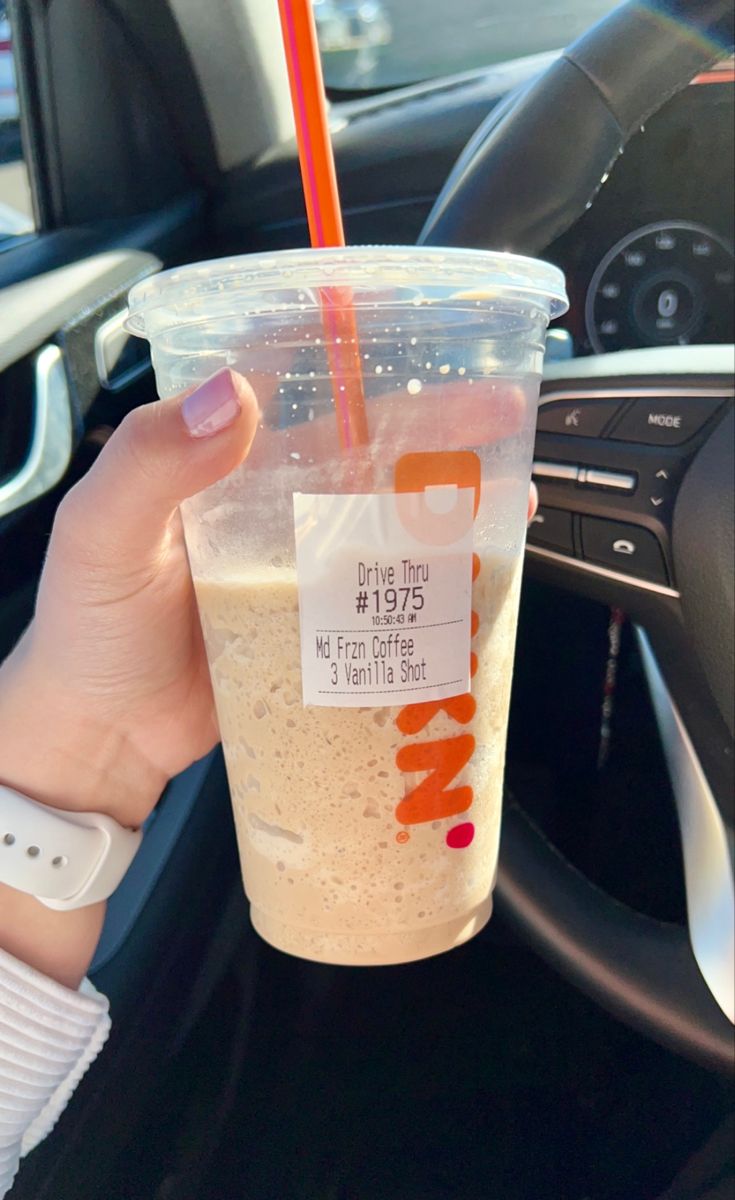 a person holding a drink in their hand while sitting in a car with the steering wheel behind them