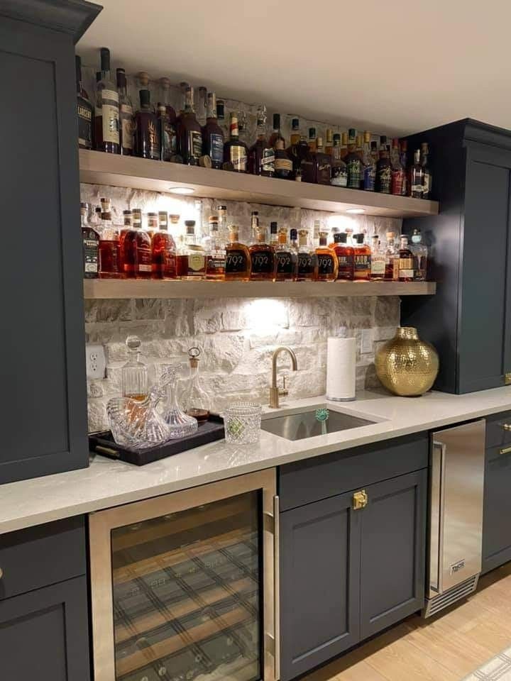 a kitchen with gray cabinets and shelves filled with liquor bottles on top of the counter