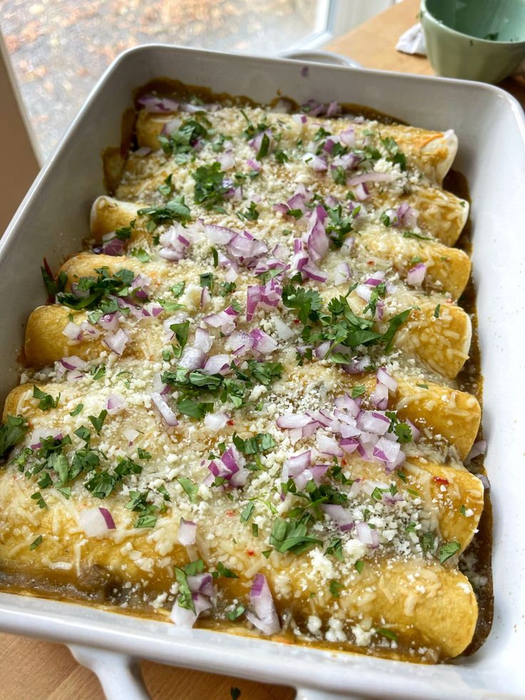 an enchilada dish in a white casserole dish on a wooden table