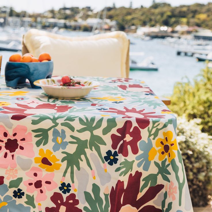 the table is covered with a colorful flowered cloth and bowl of fruit on it