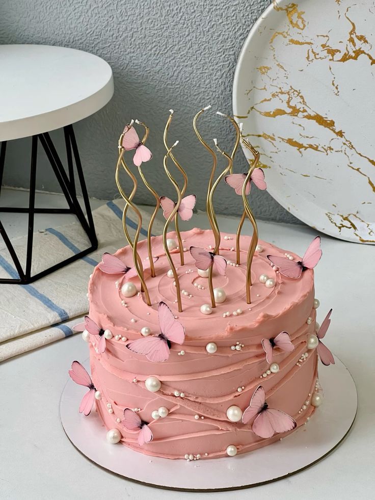 a cake with pink frosting and butterflies on it sitting on a table next to a plate