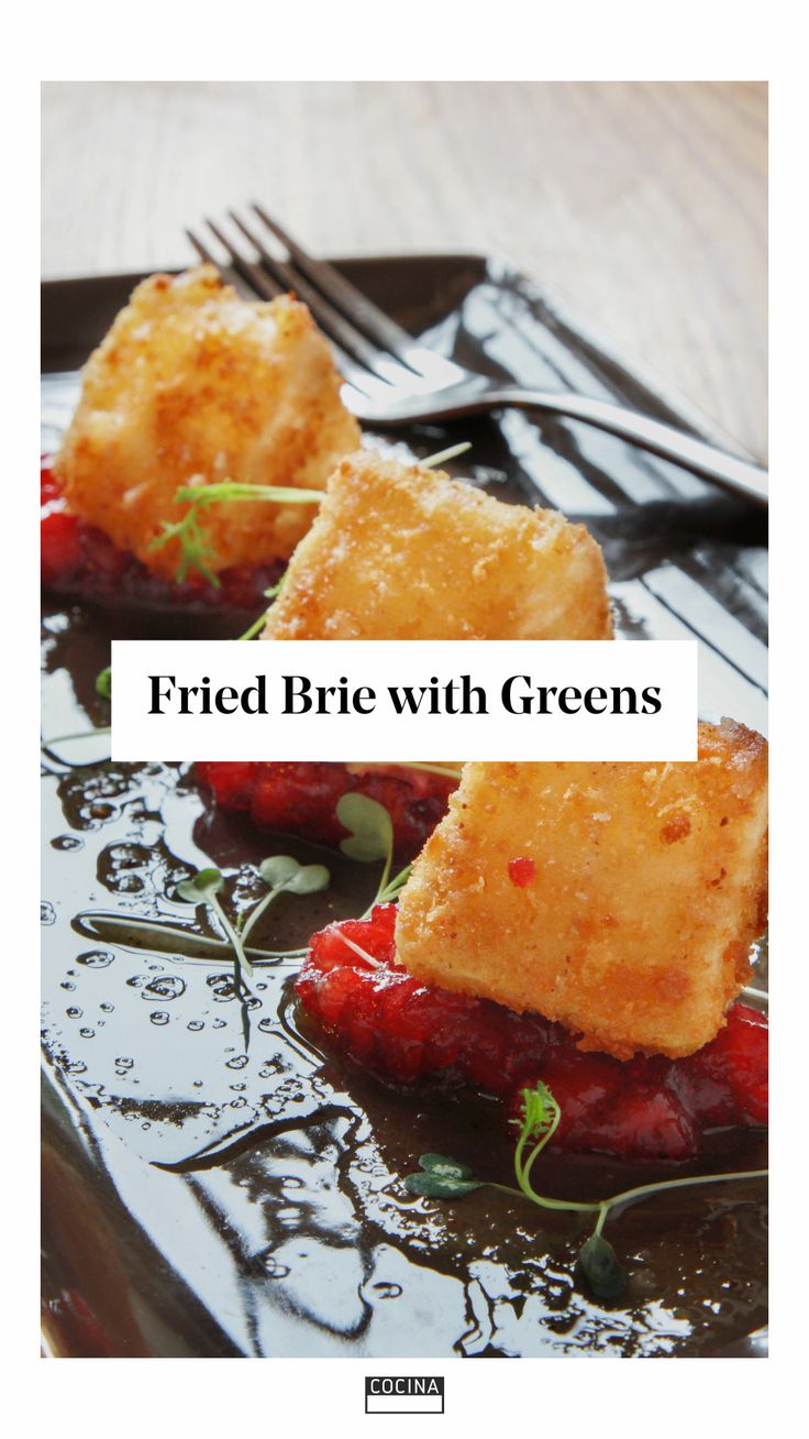 fried brie with greens on a black plate next to a fork and napkins