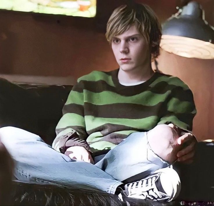 a young man sitting on top of a couch next to a lamp