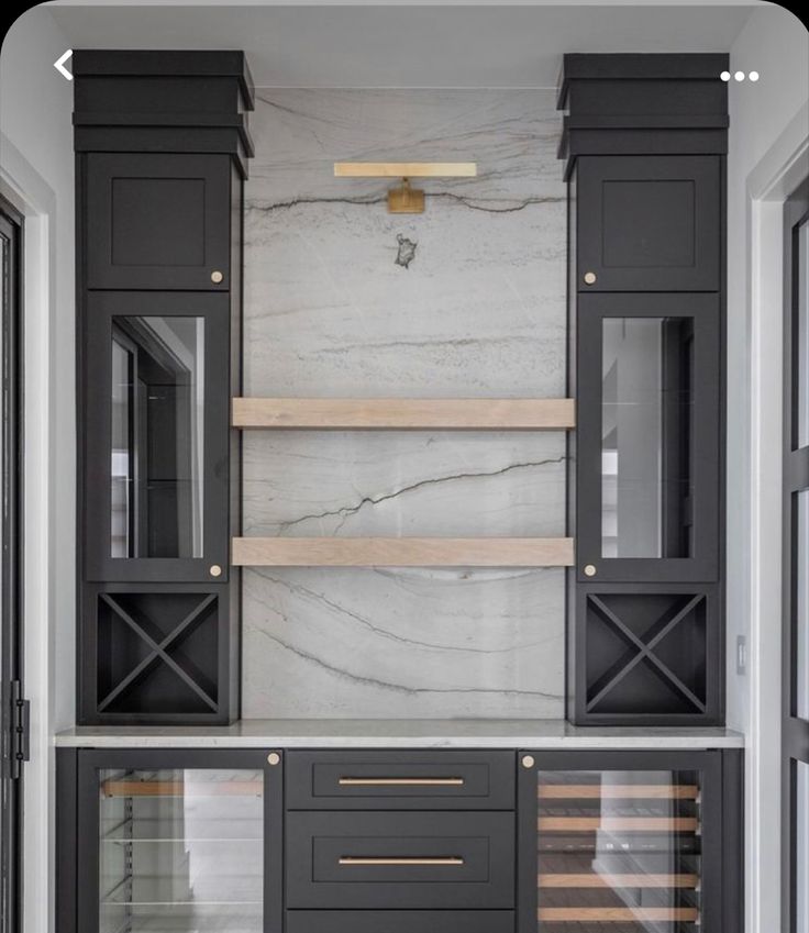 a kitchen with marble counter tops and black cabinetry, along with wooden shelves that have wine glasses on them