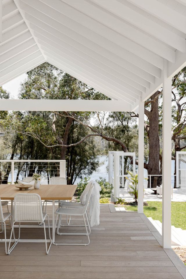 an outdoor dining table and chairs under a white pergolated roof with trees in the background