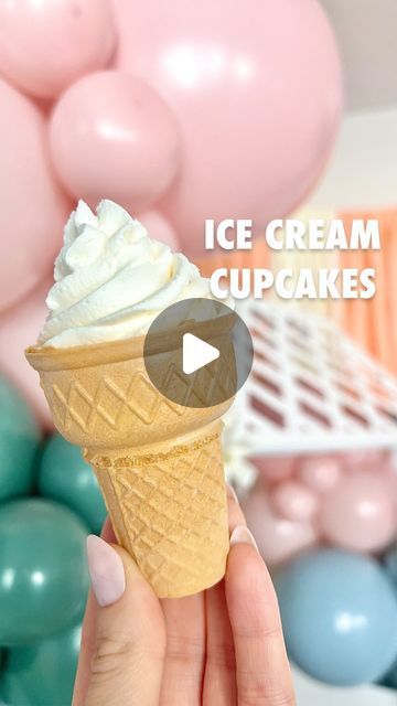 an ice cream cupcake being held up by someone's hand with balloons in the background