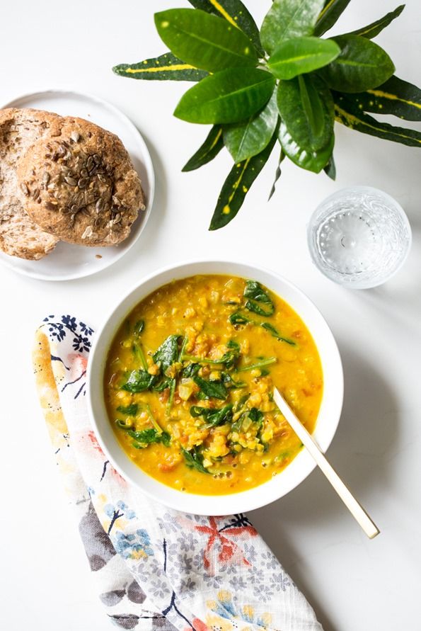 a bowl of soup with spinach and bread next to it