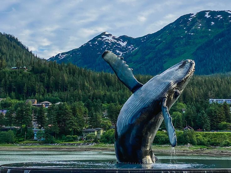 a statue of a humpback whale in the water with mountains in the background