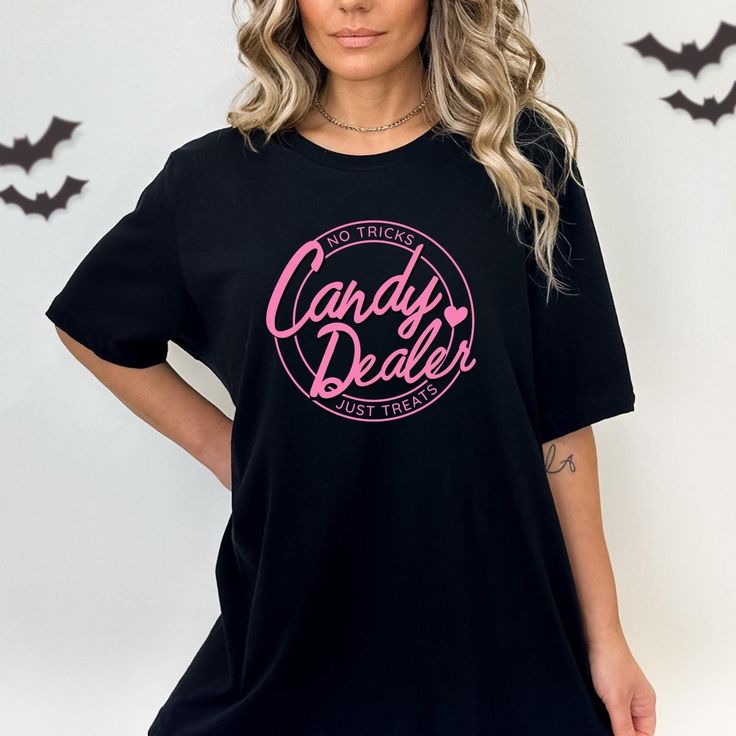 Fun, pink doll themed Halloween candy dealer T-Shirt perfect for trick-or-treating or handing out candy. Ideal for moms who want to show off their festive spirit while staying comfortable and stylish. Perfect for Halloween celebrations. P R O D U C T  F E A T U R E S :  * Unisex, Classic Fit, Jersey Short Sleeve Tee * Made with 100% lightweight cotton M E A S U R I N G   T I P : Take your favorite tee, lay it flat on a surface and measure from armpit to armpit (width) and top to bottom (length), then compare with our size chart.  C A R E   I N S T R U C T I O N S : * Machine wash cold, inside out on gentle. Lay flat to dry (or tumble dry on low heat) * Do not iron directly on graphic print. - Do not dryclean Novelty Pink Crew Neck T-shirt, Halloween Character Print Pink Top, Pink Novelty T-shirt With Funny Print, Pink Halloween Graphic Tee, Pink Novelty Crew Neck T-shirt, Pink Crew Neck Novelty T-shirt, Pink Halloween T-shirt With Letter Print, Spooky Pink T-shirt For Halloween, Pink Halloween T-shirt With Character Print