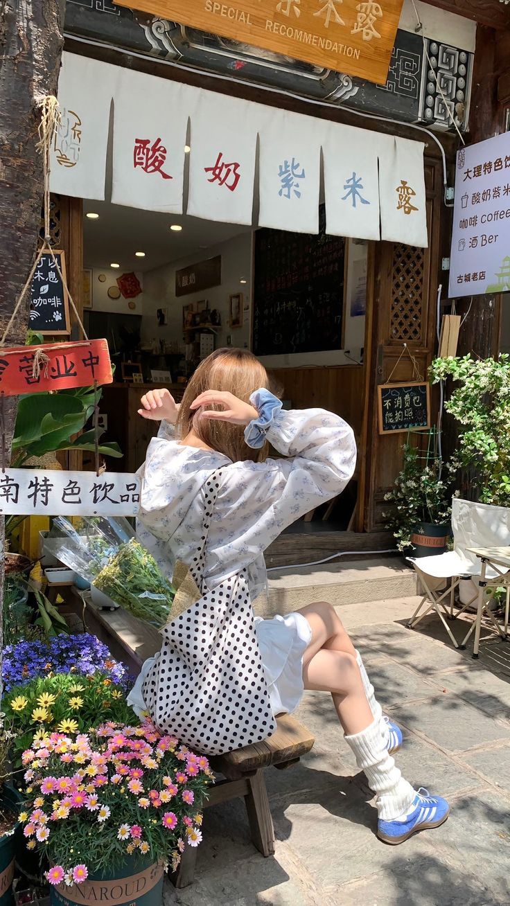 a woman sitting on a bench in front of a flower shop holding her head with both hands