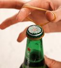 a person holding a wooden stick over a green beer bottle