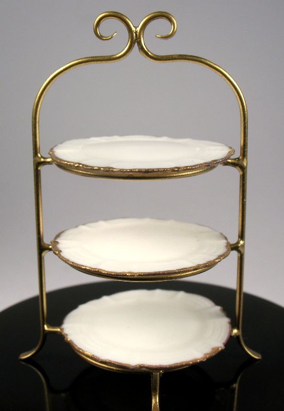 three tiered cake stand with white plates on it's bottom and gold trimmings