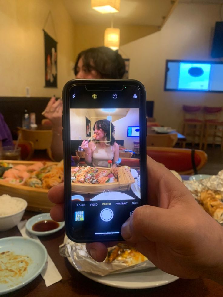 a person holding up a cell phone to take a picture of food on the table