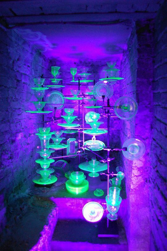 a room filled with lots of green and purple lights next to a brick wall covered in glass vases